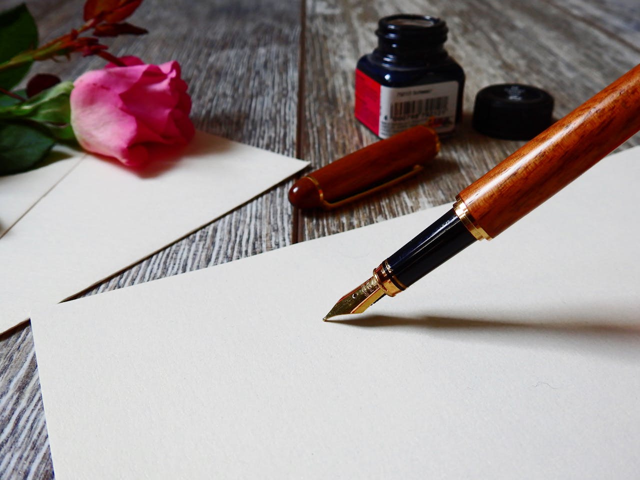 A romantic setup with a rose, fountain pen, and paper, perfect for heartfelt writing.