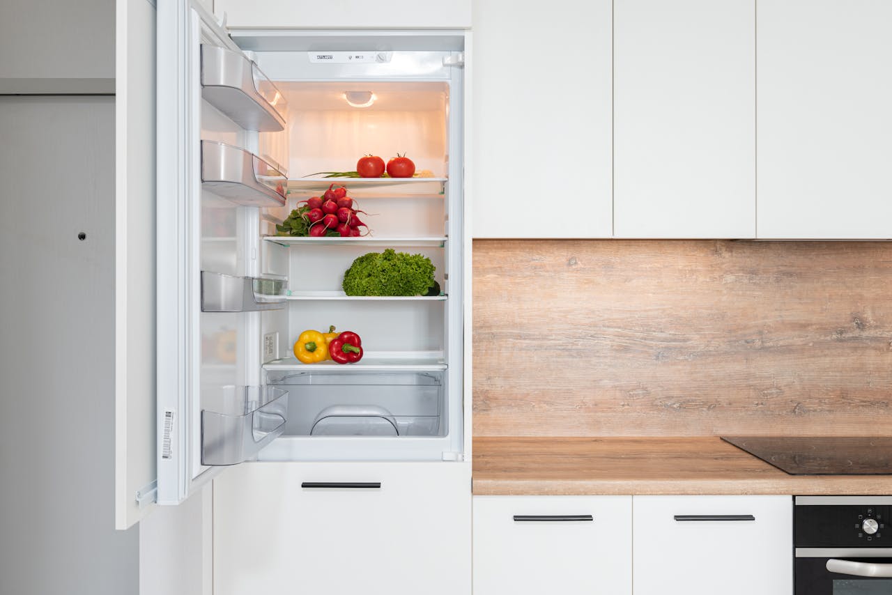 Open fridge in a sleek kitchen with fresh vegetables, perfect for healthy meals.